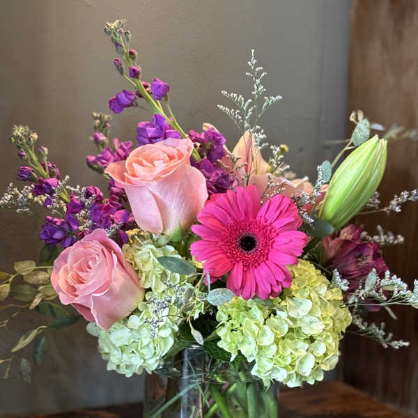 Mixed bouquet of pink roses, hot pink gerbera, purple flowers and green hydrangeas in a clear glass vase