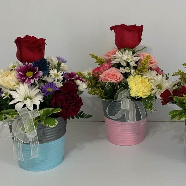 Three mixed flower arrangements in colorful tin pots with red roses on top