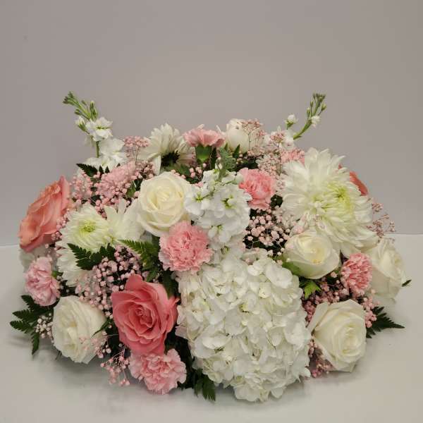 Low centerpiece of white hydrangeas, roses, and pink carnations in a soft pastel palette