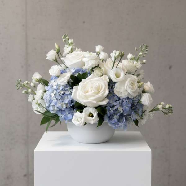 White and pale blue floral arrangement in a white bowl vase