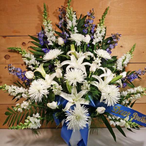 White lilies and chrysanthemums with blue ribbon on a sympathy spray