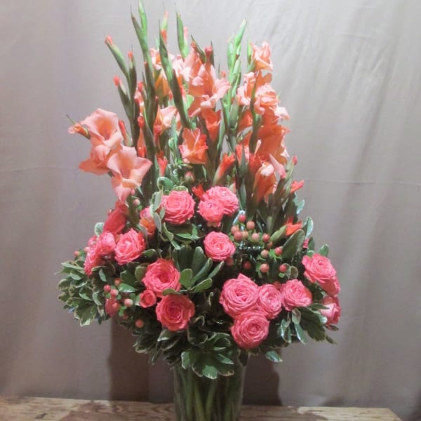 Tall arrangement of peach gladiolus and bright pink spray roses in a clear glass vase