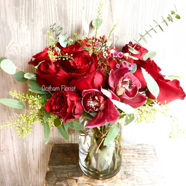 Red roses and orchids in a clear glass vase
