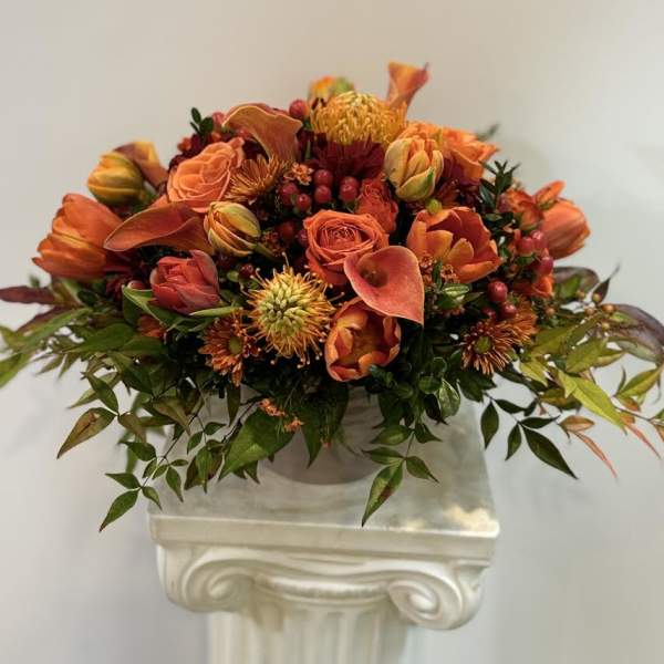 Orange floral arrangement in a white pedestal vase