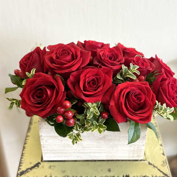 Red roses arranged in a white wooden box with berries and greenery