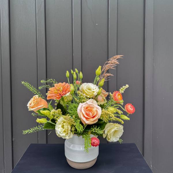 Mixed bouquet of peach, cream, and orange flowers in a white ceramic vase