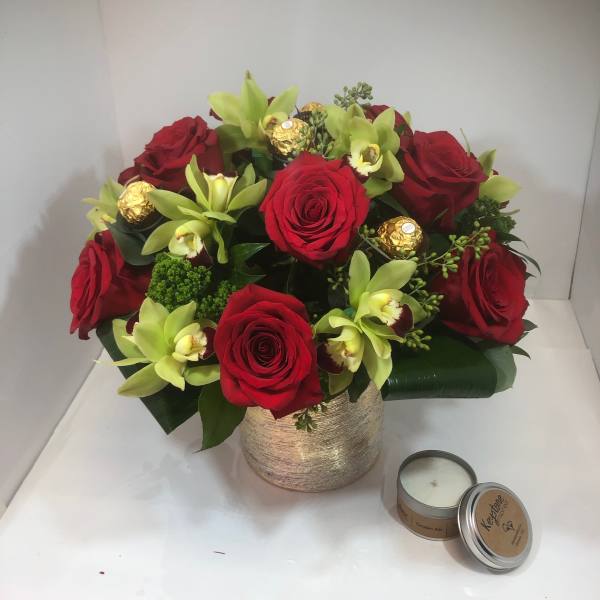 Red roses and green orchids in a gold vase with a candle beside it