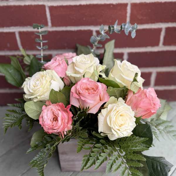 Bouquet of pink and white roses with greenery in a square container