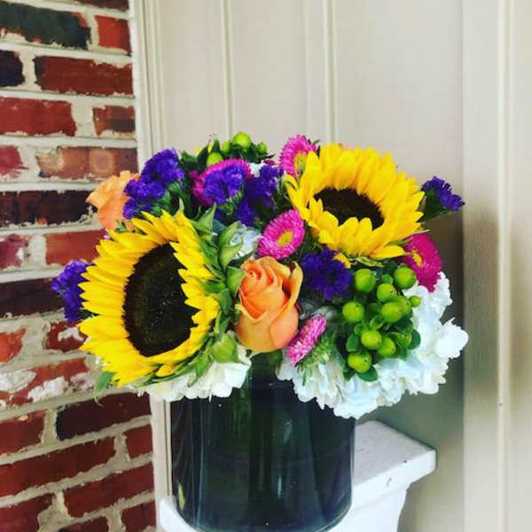 Bright mixed bouquet with sunflowers, roses, and daisies in a dark vase