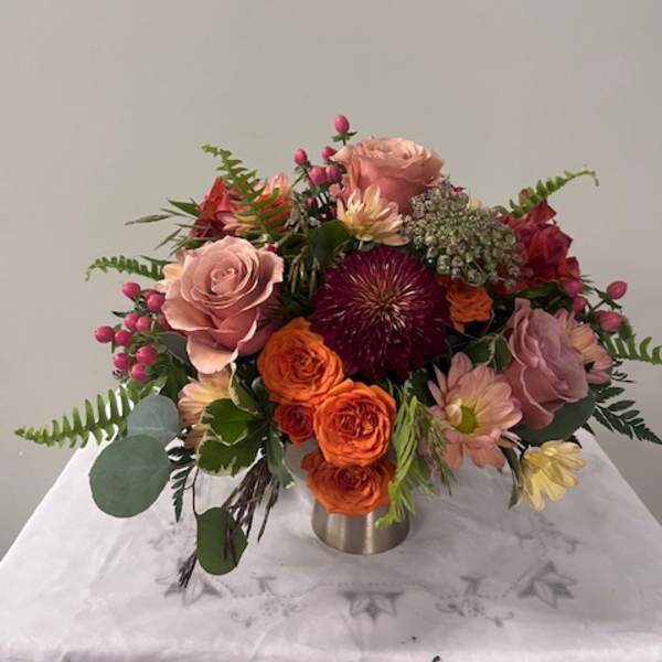 Mixed bouquet of pink, orange, and red flowers in a low metal vase