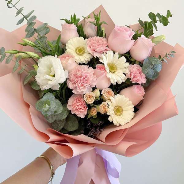 Handheld bouquet of pink roses, white gerbera daisies, and carnations wrapped in pink paper