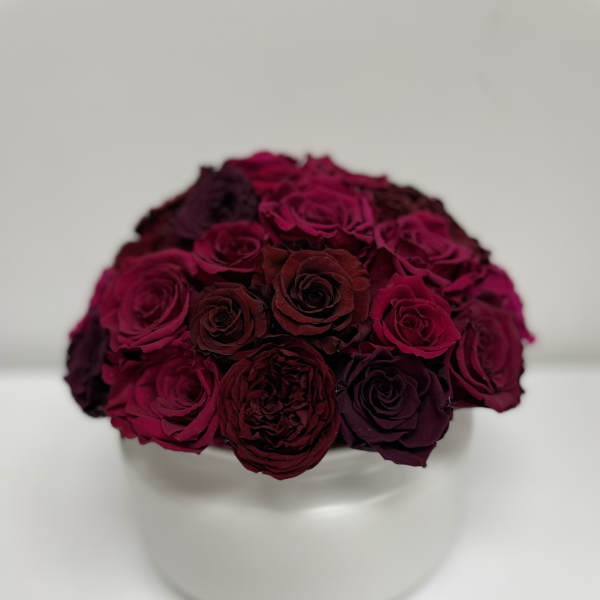 Compact bouquet of deep burgundy roses in a white vase