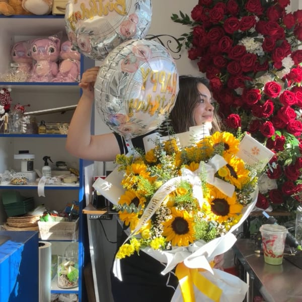 Woman holding a sunflower bouquet and two birthday balloons