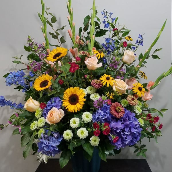 Large mixed arrangement with sunflowers, roses, hydrangeas, and assorted blooms in a dark container