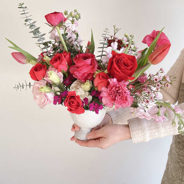 Handheld bouquet of red and pink flowers in a white vase