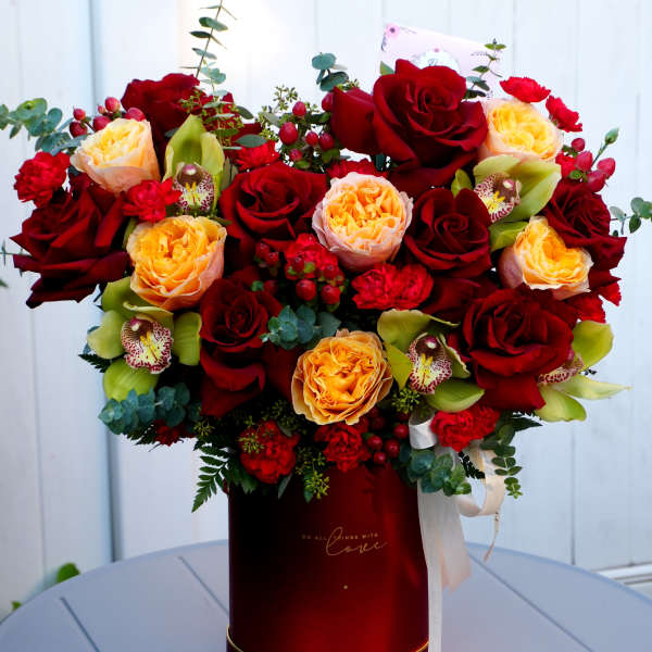 Red and peach roses arranged in a tall red box with ribbon