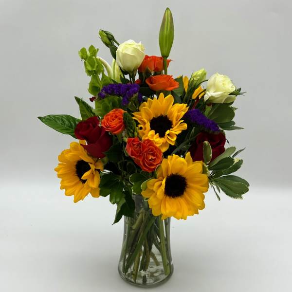 Mixed bouquet of sunflowers, roses, and lilies in a glass vase