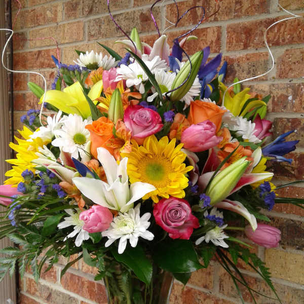 Colorful mixed bouquet with lilies, roses, daisies, and a sunflower in a glass vase