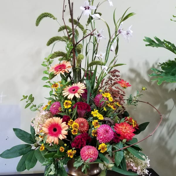 Tall mixed arrangement of pink and orange blooms with yellow accents in a gold pedestal vase