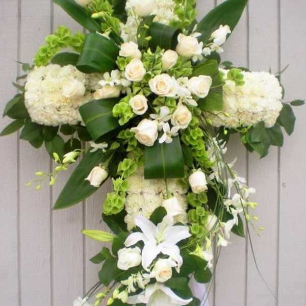 Tall white floral cross with roses, lilies, and green accents on a standing easel