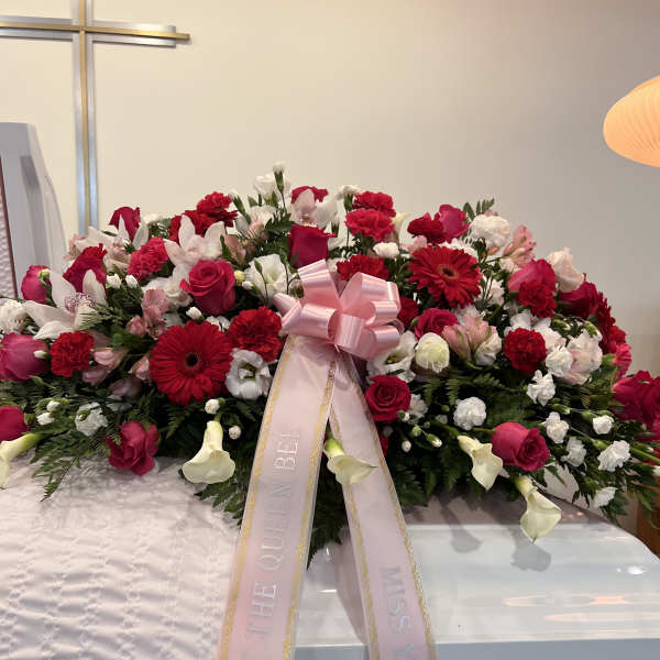 Large pink and red funeral spray with ribbon on a casket