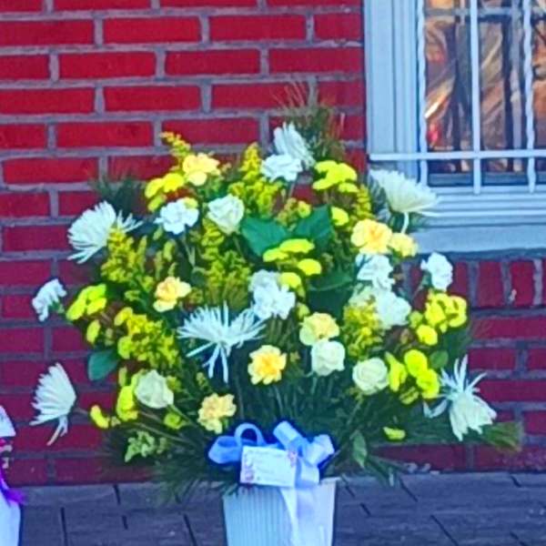 Yellow and white floral arrangement in a white vase with a blue ribbon