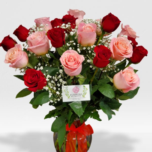 Arrangement of red and pink roses with white filler flowers in a glass vase with a red bow