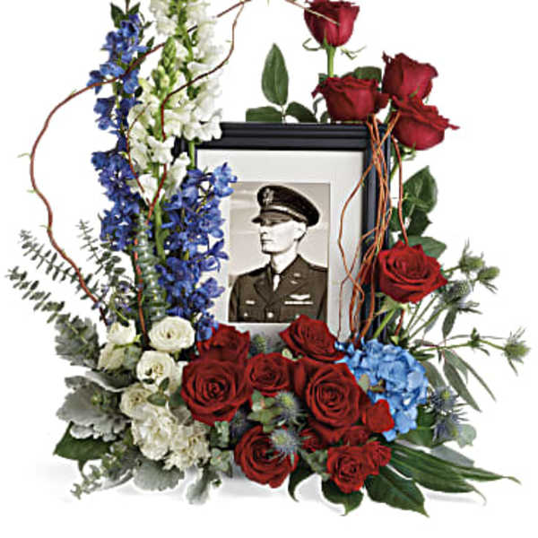 Floral tribute around a framed portrait with red roses and blue and white blooms
