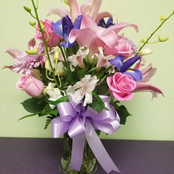 Pink and purple mixed bouquet in a glass vase with a lavender ribbon