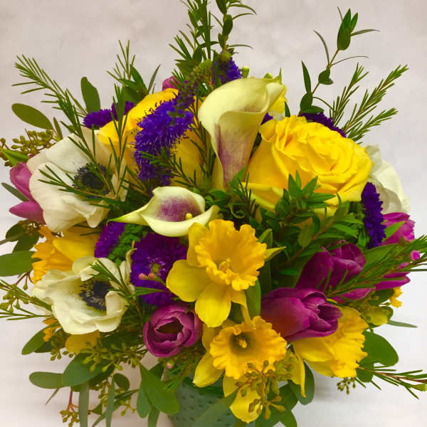 Mixed bouquet with yellow roses, calla lilies, and purple flowers in a green vase