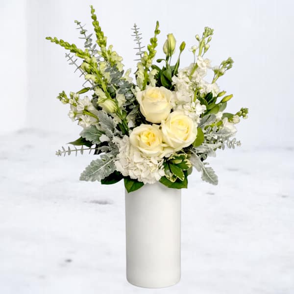 White roses and white flowers arranged in a tall white vase