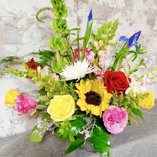 Colorful mixed flower arrangement in a metal container with roses and sunflowers