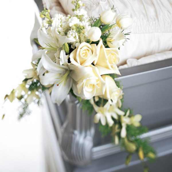 White floral bouquet with roses and lilies draped over a gray casket