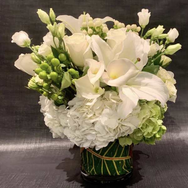White floral arrangement with calla lilies, roses, and hydrangeas in a green vase