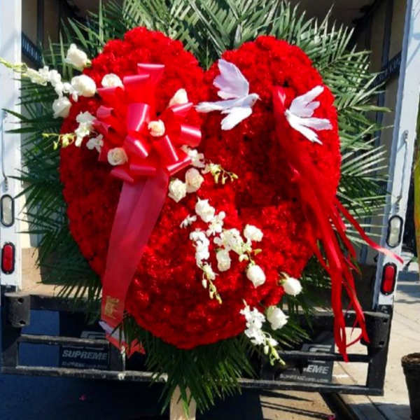 Large red heart-shaped floral tribute with white accents on a stand