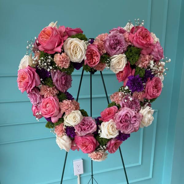 Heart-shaped floral wreath of pink, white, and purple roses on a stand