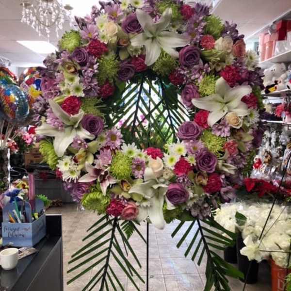Large floral wreath with lilies, roses, and purple blooms on a stand