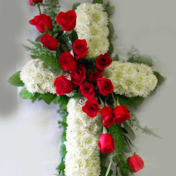 Standing floral cross of white blooms with cascading red roses on a metal easel