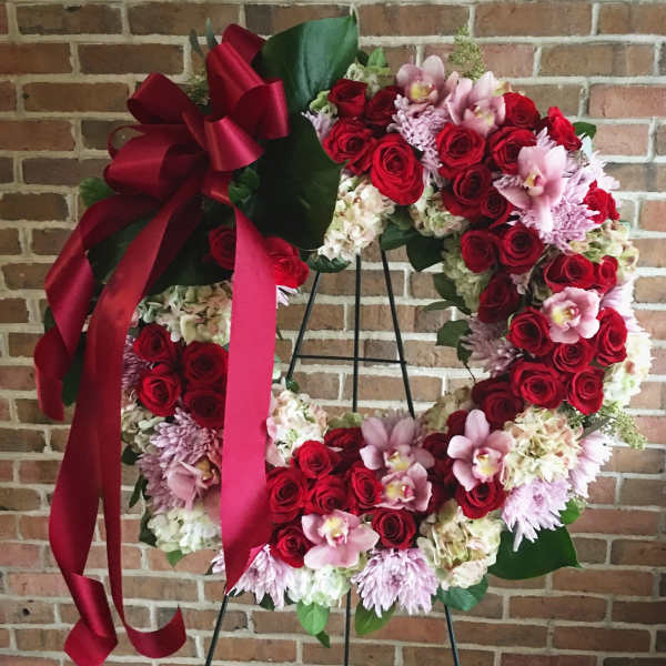 Heart-shaped floral wreath with red roses, pink orchids, and a burgundy ribbon