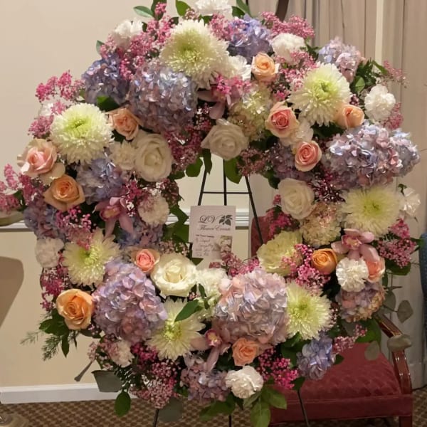 Large pastel floral wreath on a stand with roses, hydrangeas, and mums