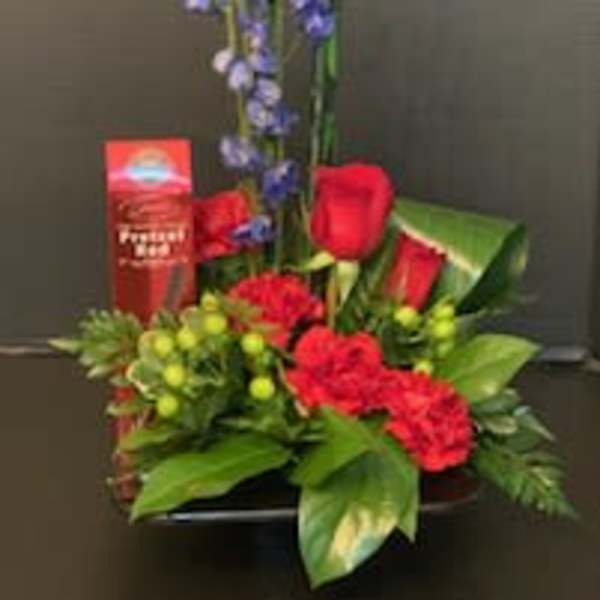 Red roses and blue flowers arranged in a low basket with a tall accent stem