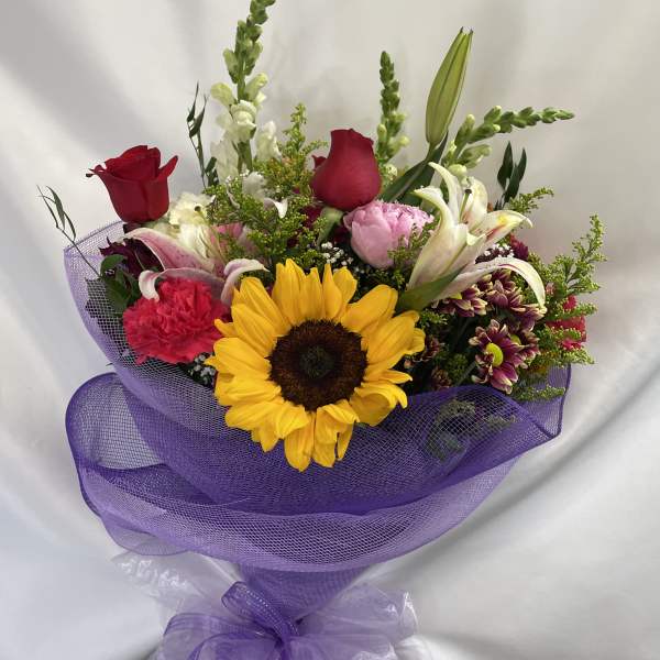 Mixed bouquet with a sunflower, roses, lilies, and purple wrapping
