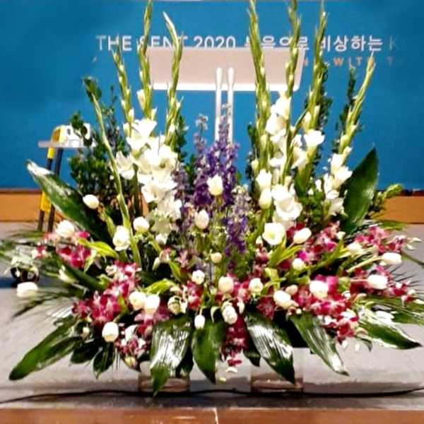 Large stage arrangement with white spikes, purple flowers, and pink orchids in a wide fan shape
