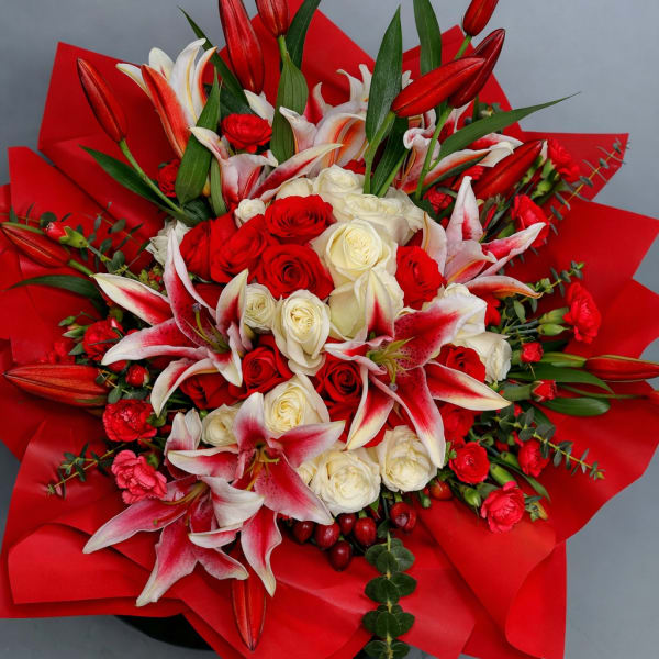 Bouquet of red and white roses with pink lilies wrapped in red paper