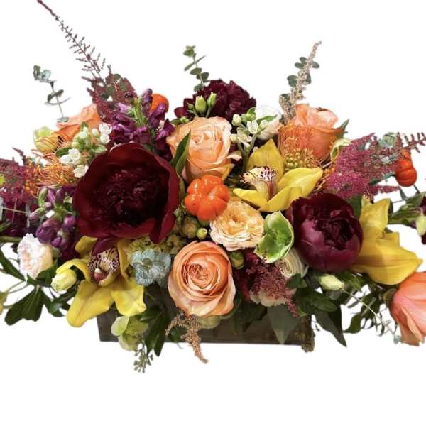 Mixed bouquet of roses, lilies, and burgundy blooms in a low rectangular container