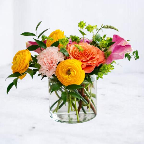 Mixed bouquet of yellow, peach, pink, and green flowers in a clear glass vase