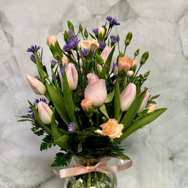 Pink tulips and peach carnations in a glass vase with a ribbon