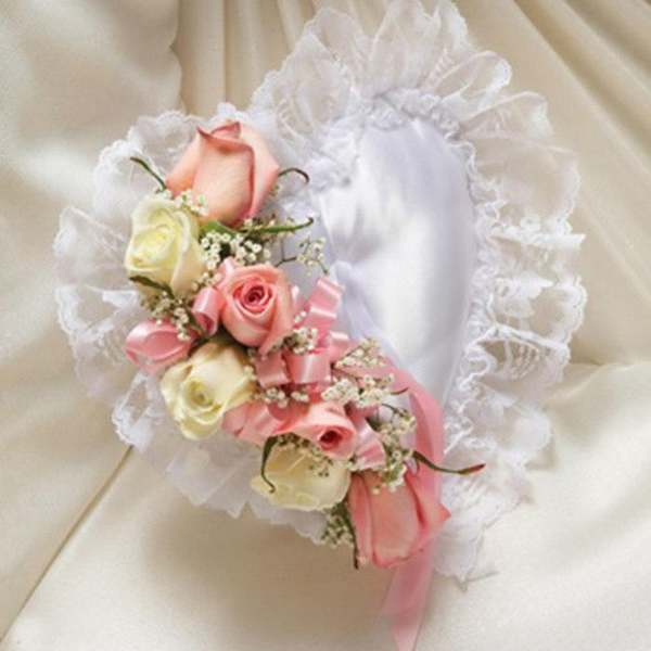 Heart-shaped white satin pillow with lace trim and pink and ivory roses on one side