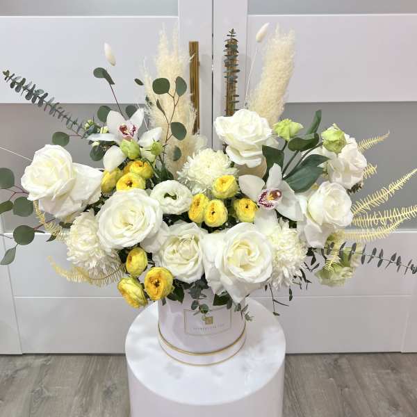 White and yellow floral arrangement in a round box