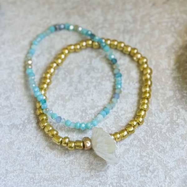 Two beaded bracelets with blue and gold beads and a white shell charm